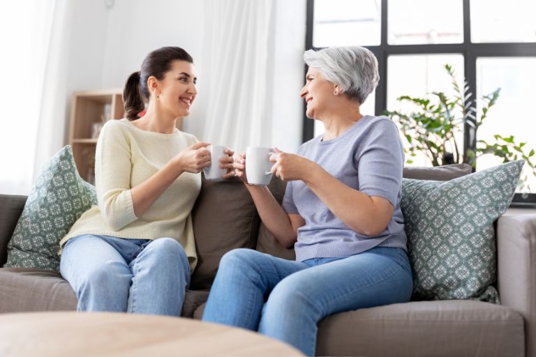 A mother and adult daughter talking and drinking tea on a sofa