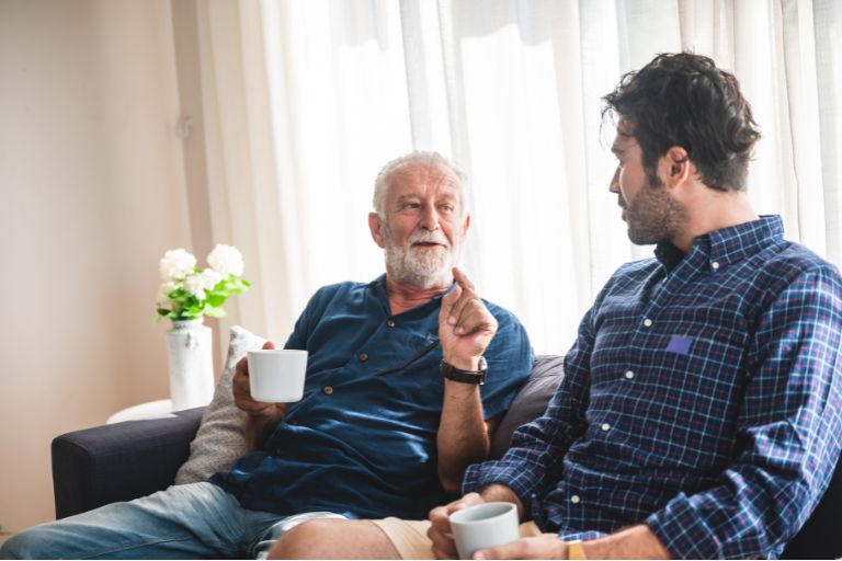Older man and son chatting and having a cup of tea on a sofa