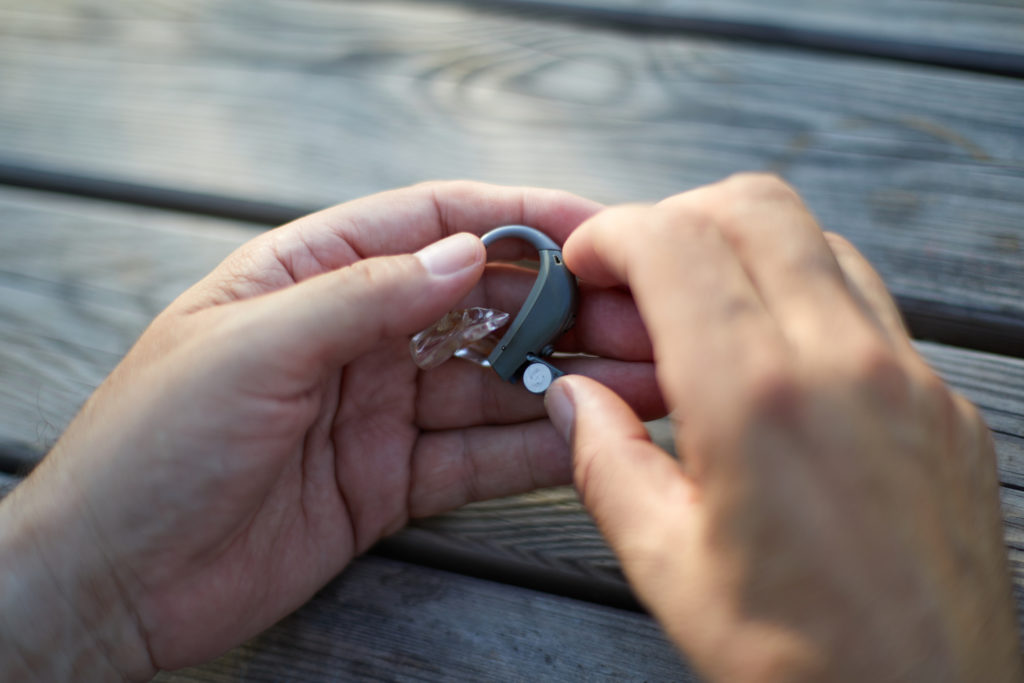 Close up of white hands changing a hearing aid battery on a wooden picnic table