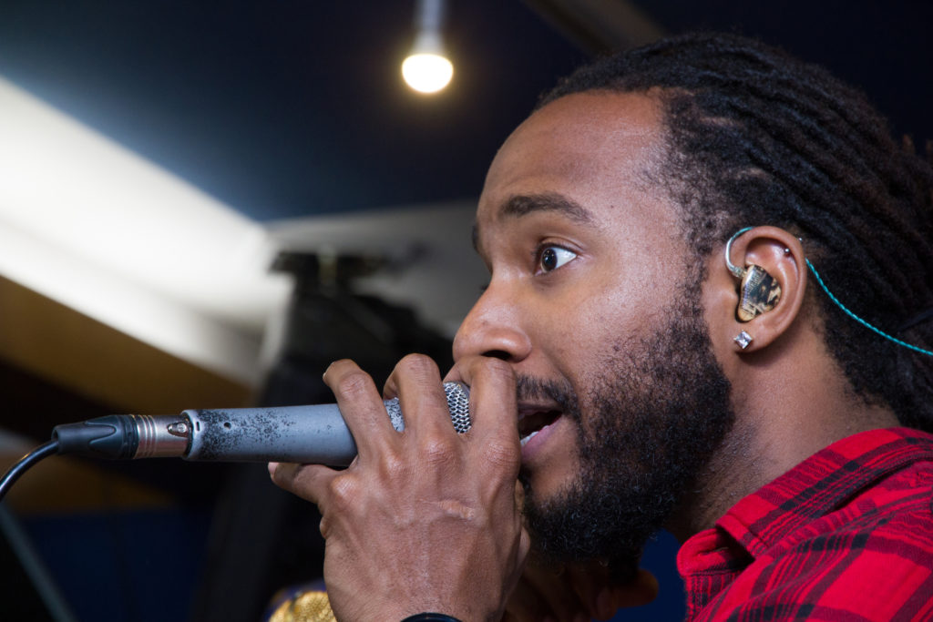A black man with a digital musician ear plug singing